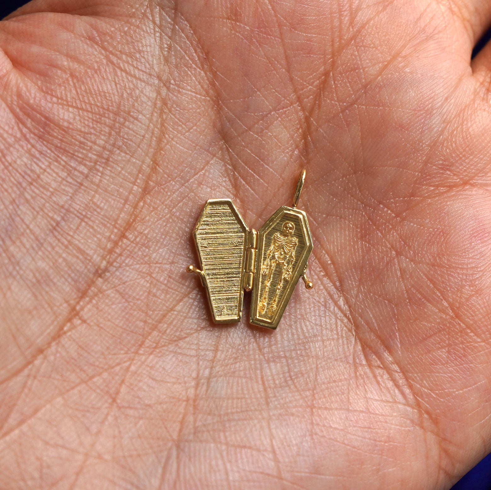 An open solid gold Coffin Charm for chain resting in a model's palm