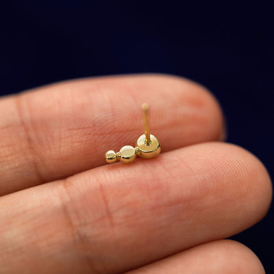 A yellow gold Graduated Ball Earring laying facedown on a model's fingers to show the underside view