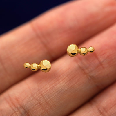 A pair of solid 14k yellow gold Graduated Ball Earring in between a model's fingers