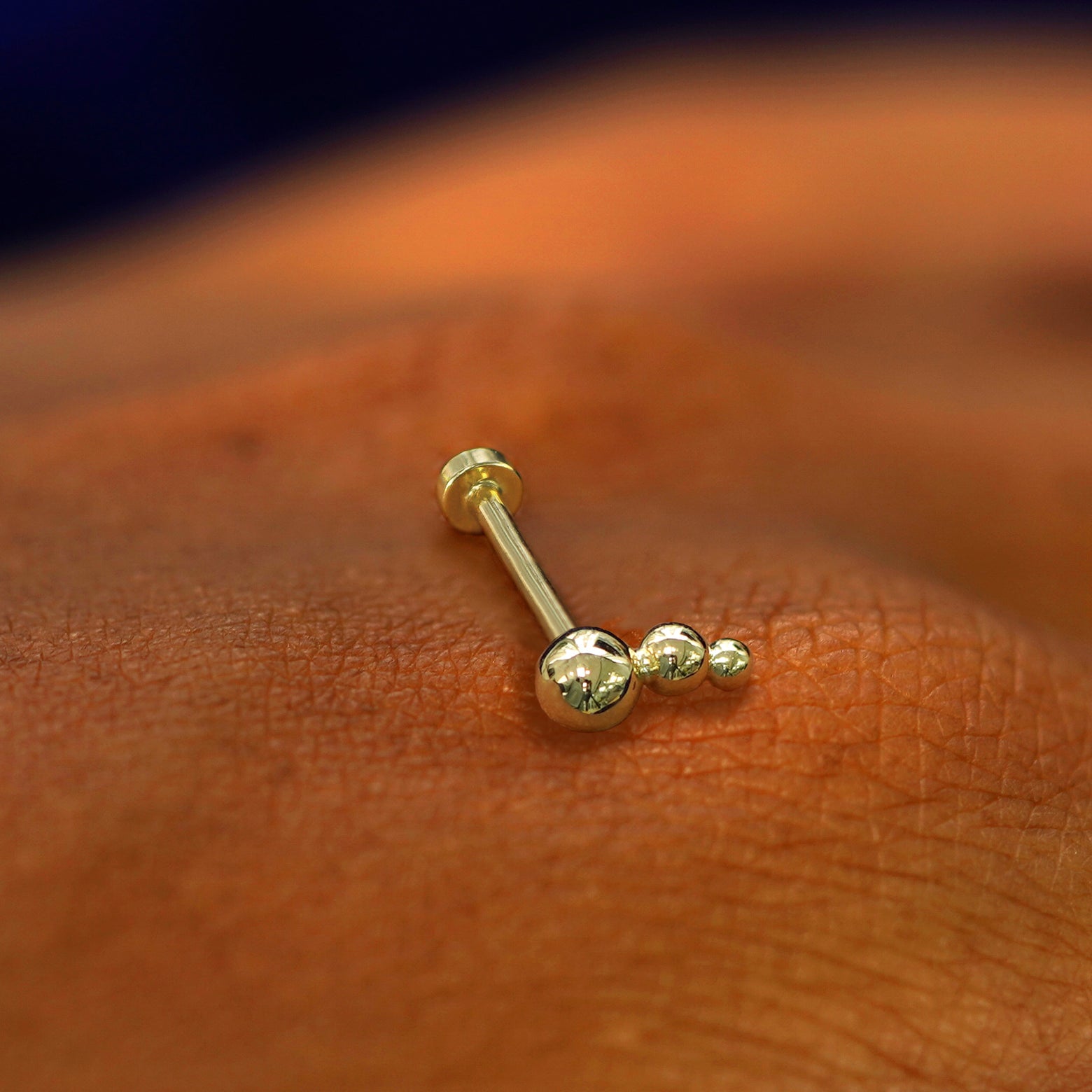 "A yellow gold Graduated Ball Flatback Piercing laying on the back of a model's hand "