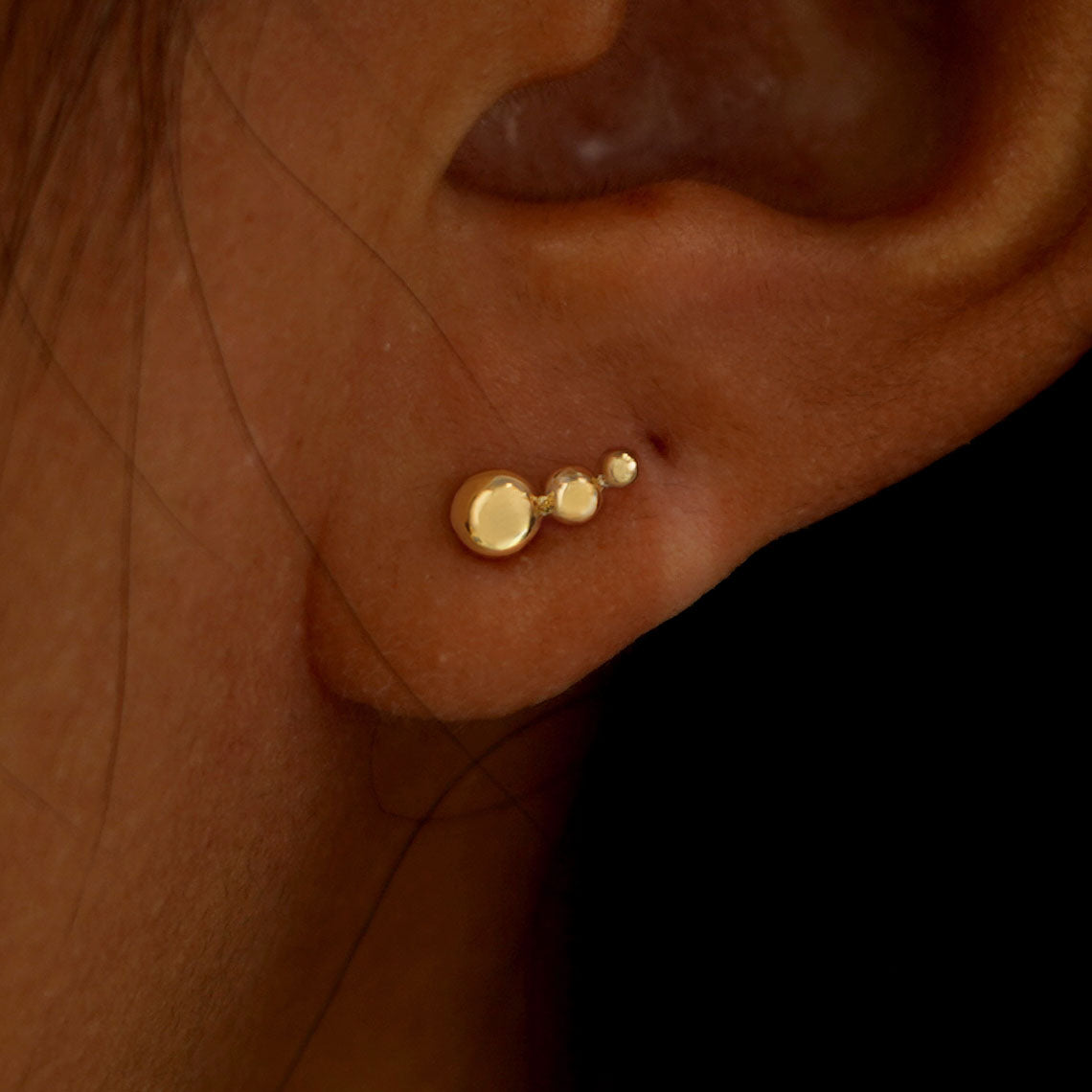 Close up view of a model's ear wearing a yellow gold Graduated Ball Flatback Piercing