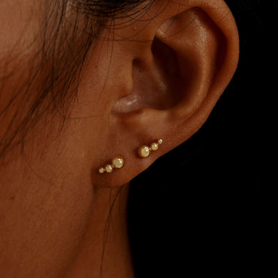 A model's ear wearing two 14k gold Graduated Ball Flatback Piercings in two lobe piercings