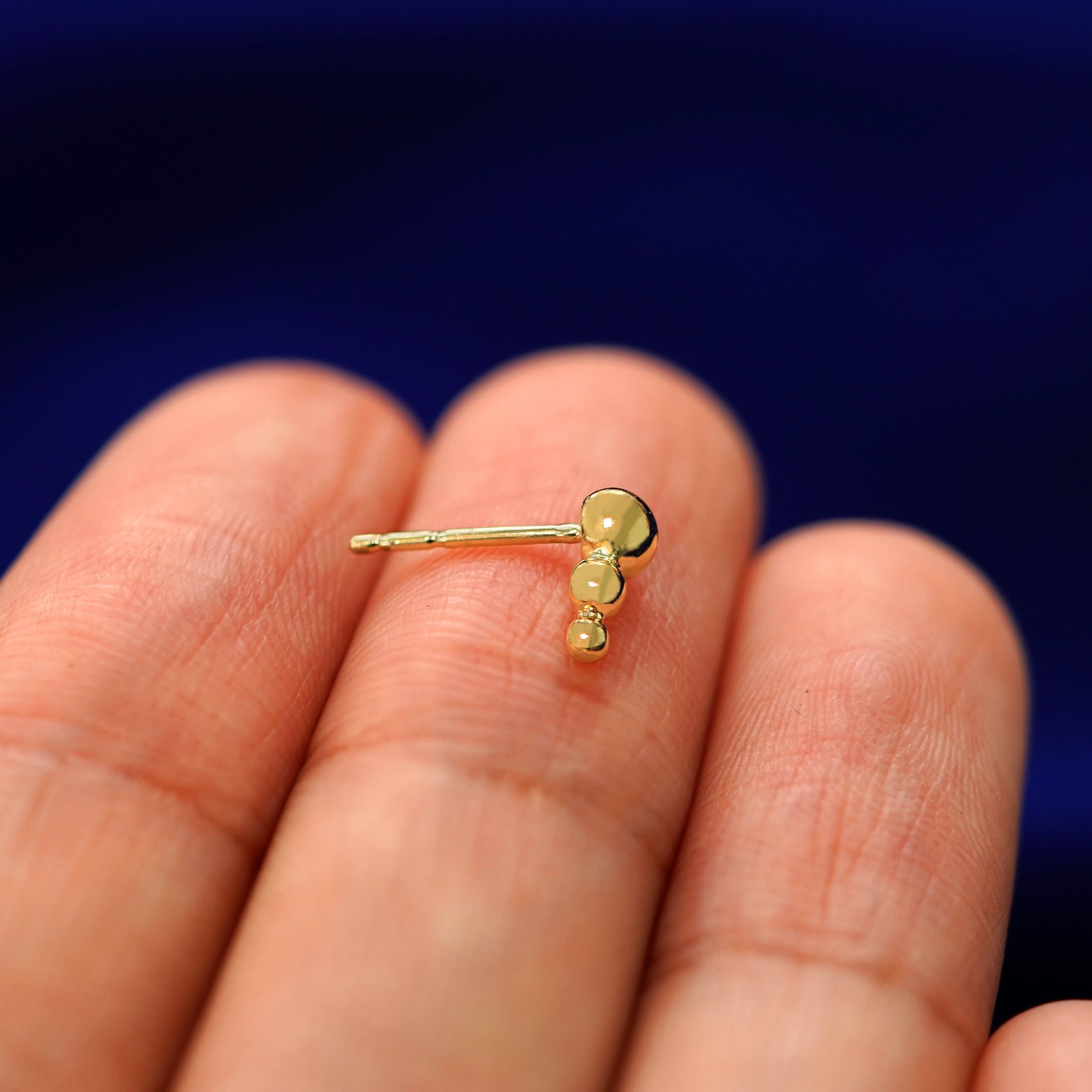 A 14k gold Graduated Ball Earring sitting sideways on a model's fingertips to show detail