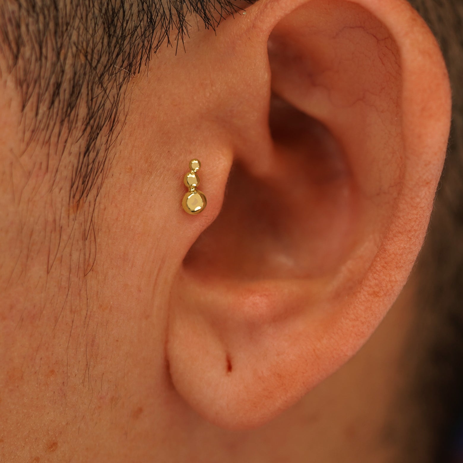 Close up view of a model's ear wearing a 14k yellow gold Graduated Ball Flatback as a tragus piercing