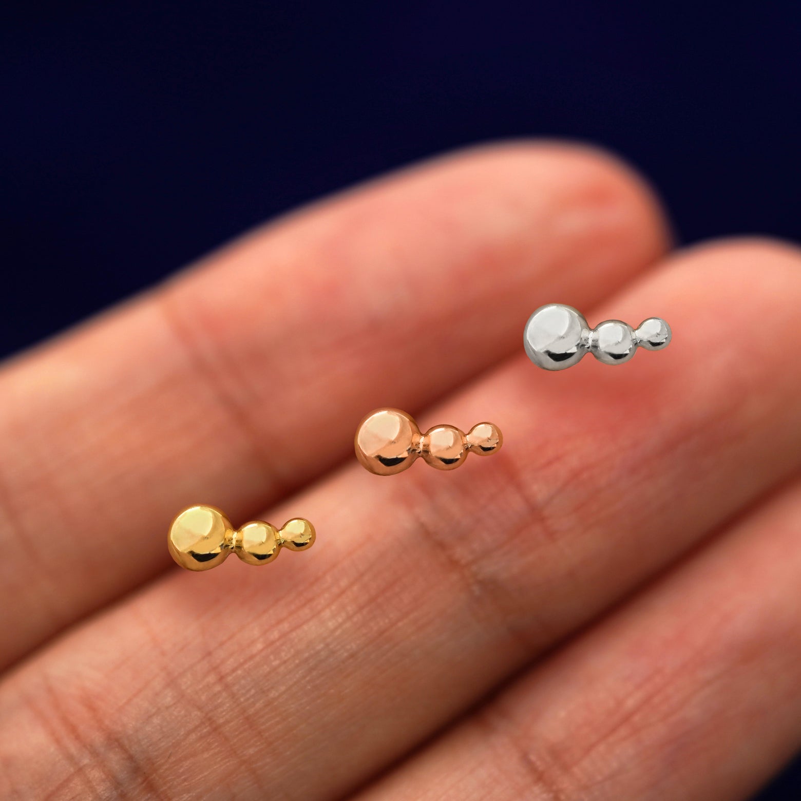 Three versions of the Graduated Ball Flat Back showing options of yellow, rose, and white gold in between a model's fingers