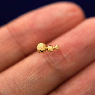 A solid 14k yellow gold Graduated Ball Earring in between a model's fingers