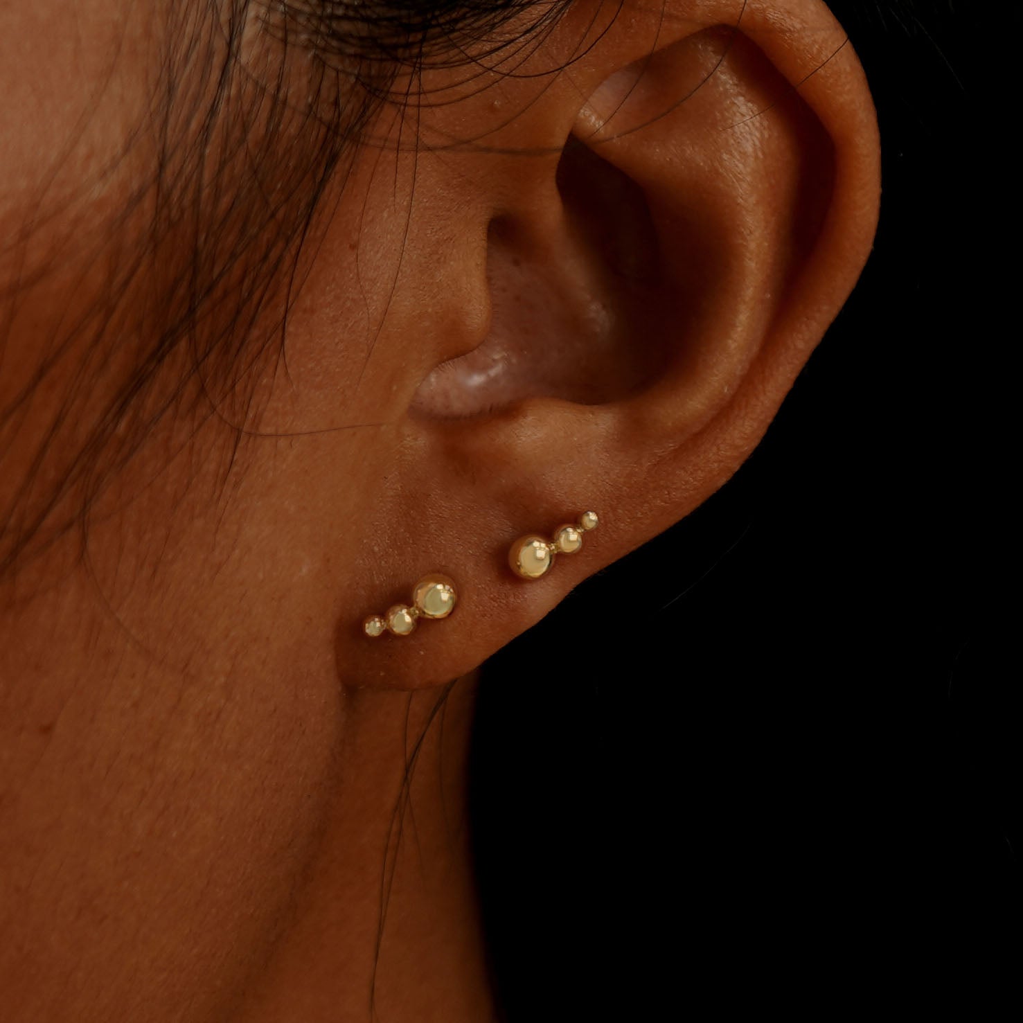 A model's ear wearing two 14k gold Graduated Ball Earrings in two lobe piercings