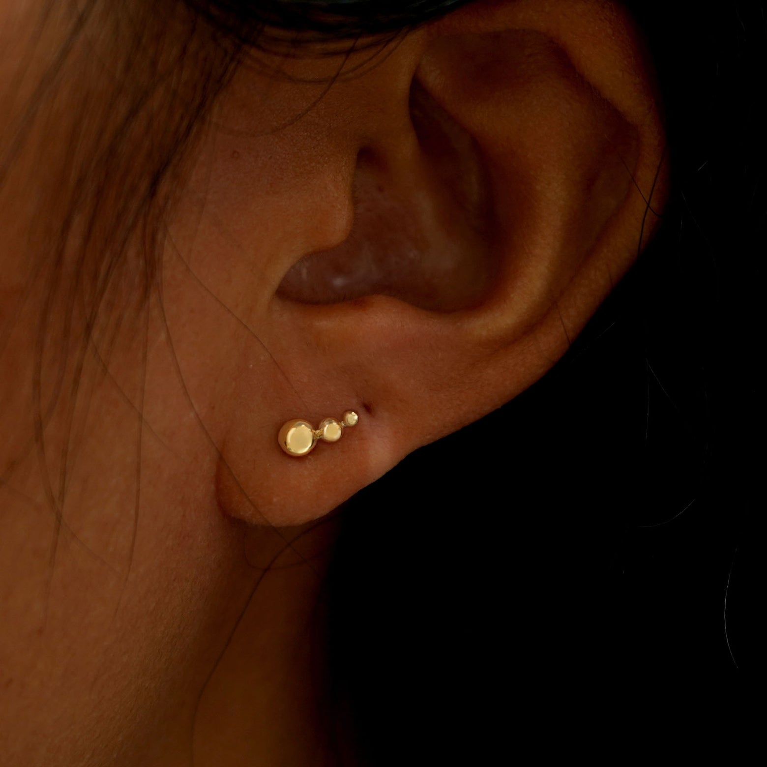 A model's ear wearing a solid yellow gold Graduated Ball Earring