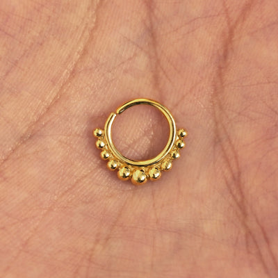 A model's hand holding a 14 karat yellow gold Pierced Beaded Septum