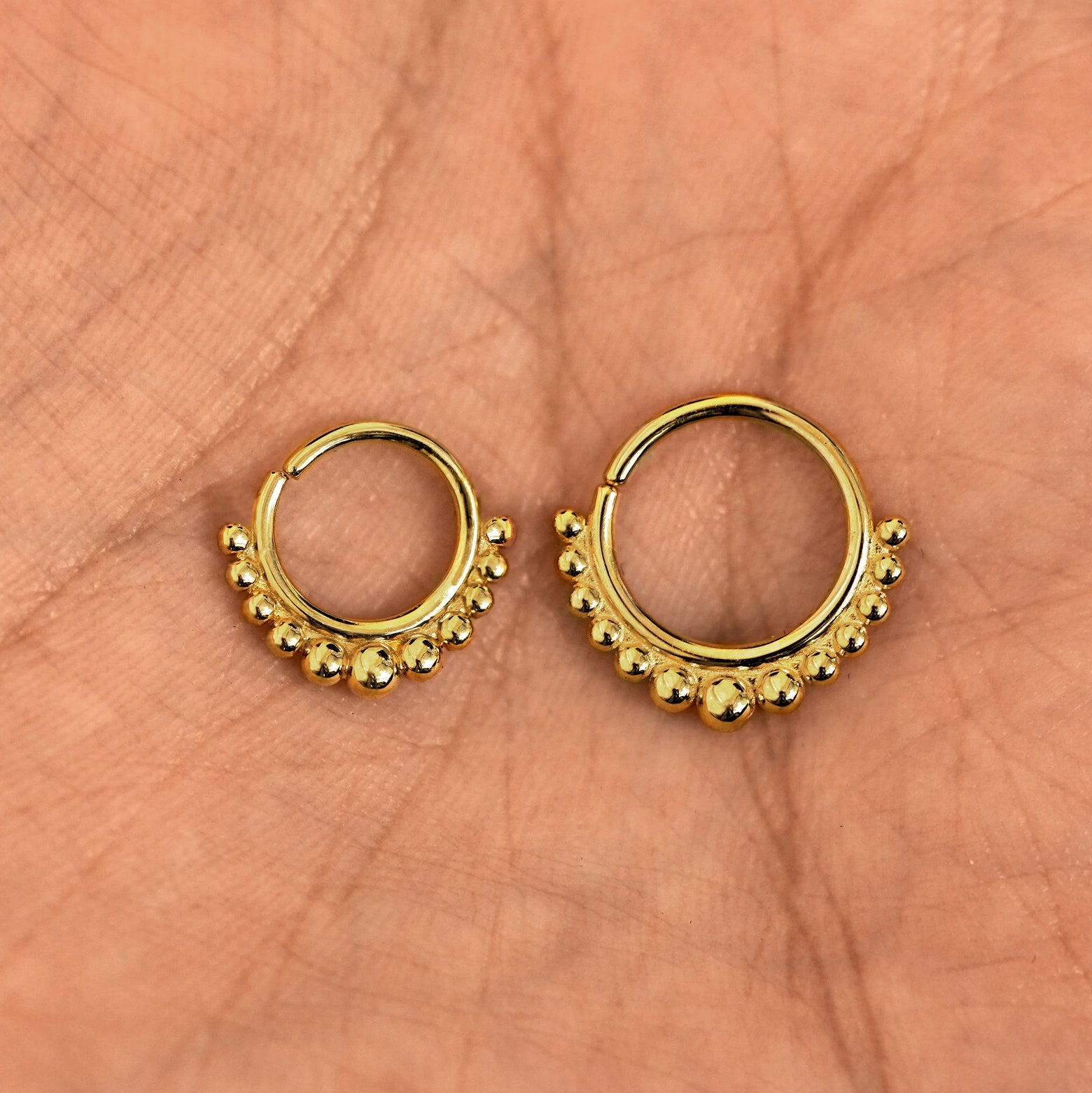 A model's palm holding two versions of the pierced Beaded Septum showing the 8mm and 10mm sizes