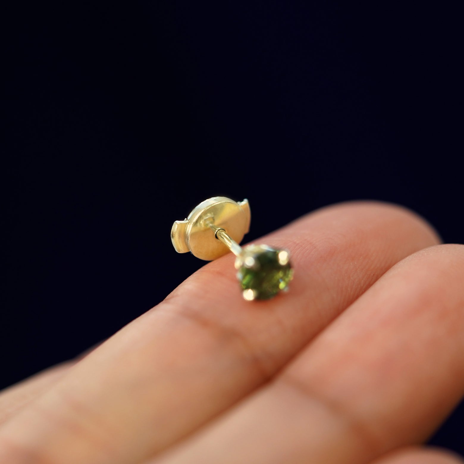 A solid gold Green Sapphire Pressure Lock Earring tilted on a model's fingertip to show the pressure lock backing on the post