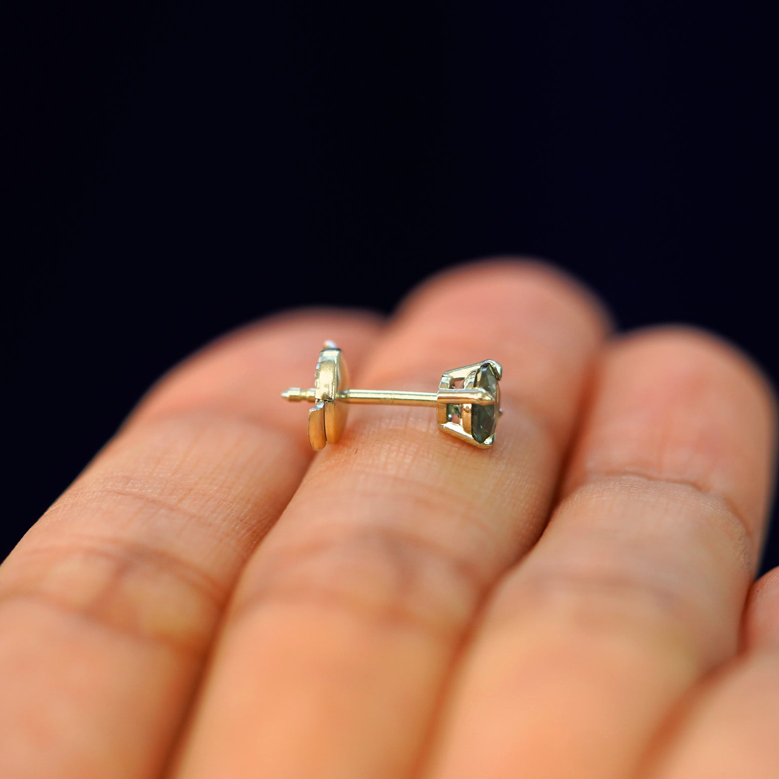 A 14k gold Green Sapphire Pressure Lock Earring resting sideways on a model's fingertips to show detail