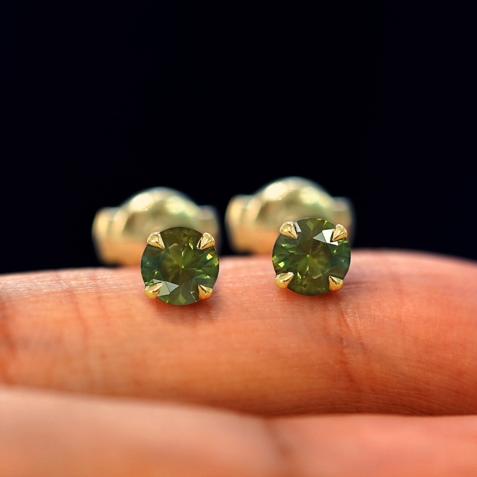 A pair of solid yellow gold Green Sapphire Pressure Lock Earrings resting on a model's fingertip