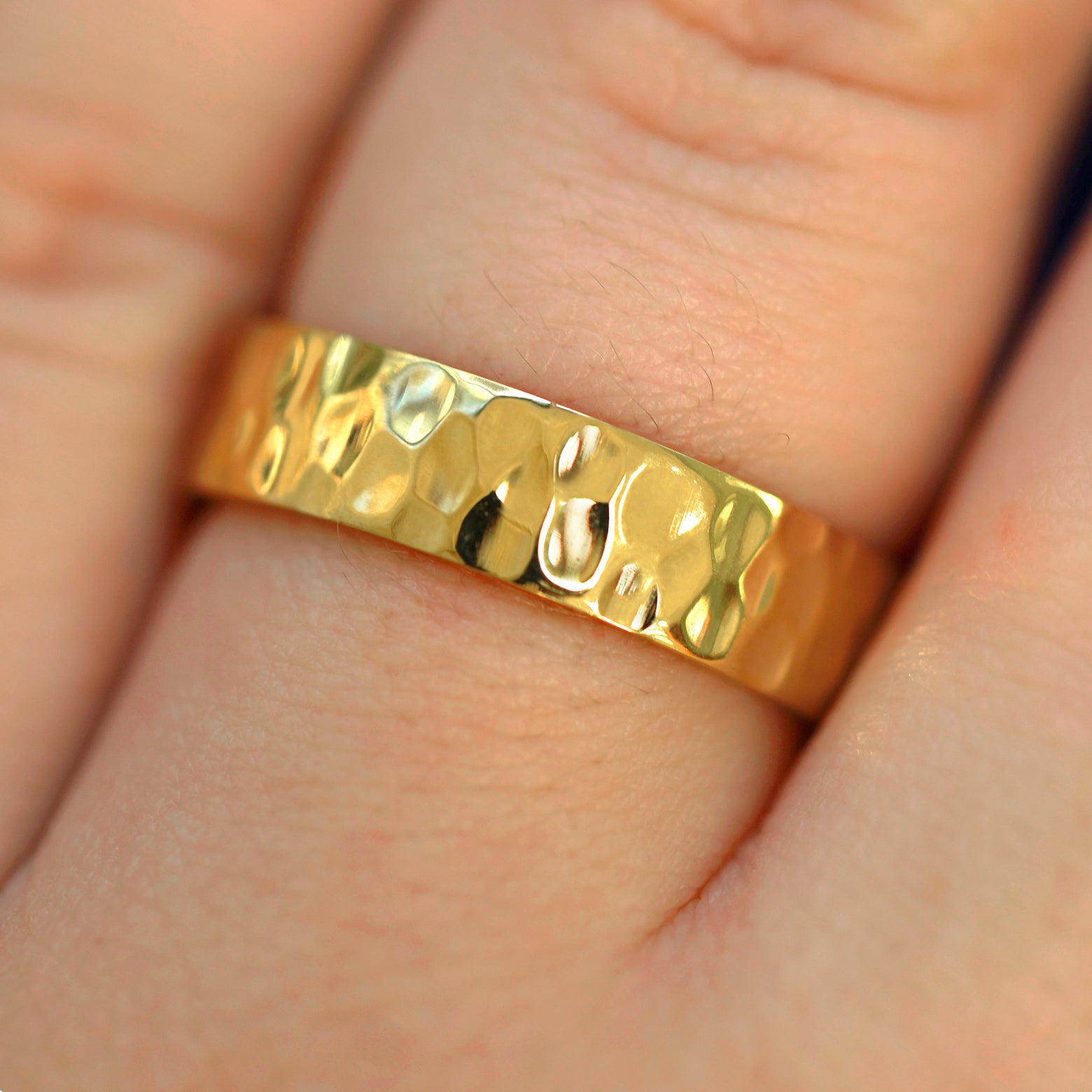 Close up view of a model's fingers wearing a 14k yellow gold Industrial Hammered Band