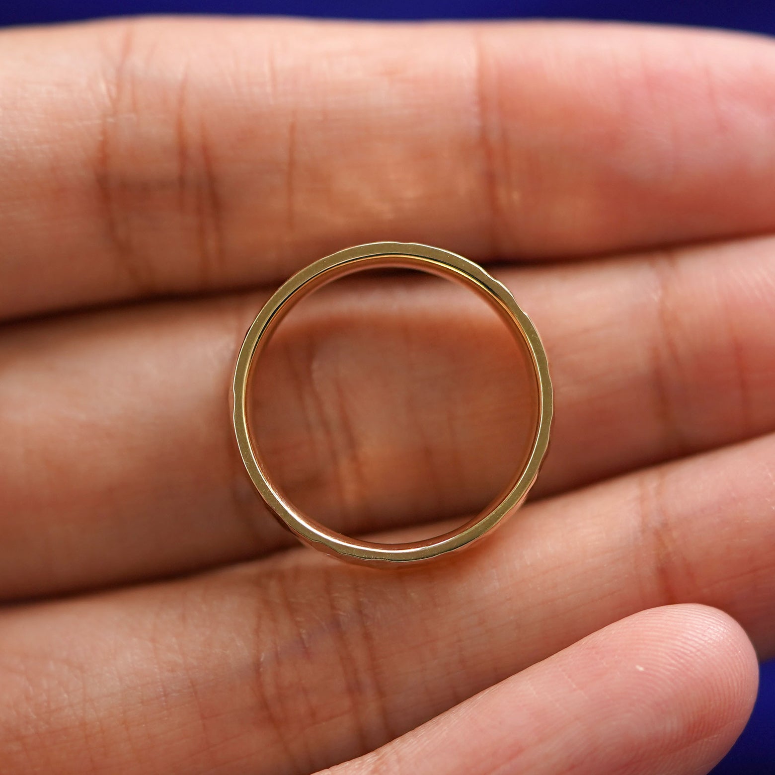 A yellow gold Industrial Hammered Band in a model's hand showing the thickness of the band