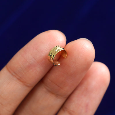 Front view of a solid yellow gold Thick Hammered Cuff earring resting on a model's fingertips