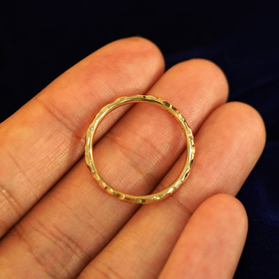 A yellow gold Curvy Hammered Band in a model's hand showing the thickness of the band