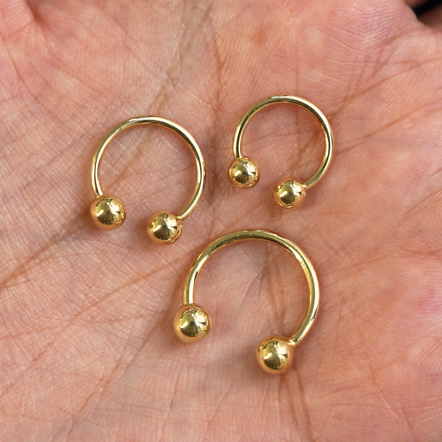 Small, Medium, and Large Horseshoe Piercings placed in a model's hand to show size difference