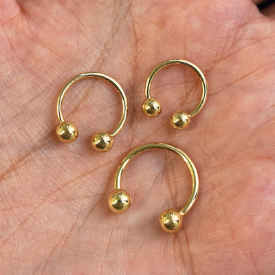 Small, Medium, and Large Horseshoe Piercings placed in a model's hand to show size difference