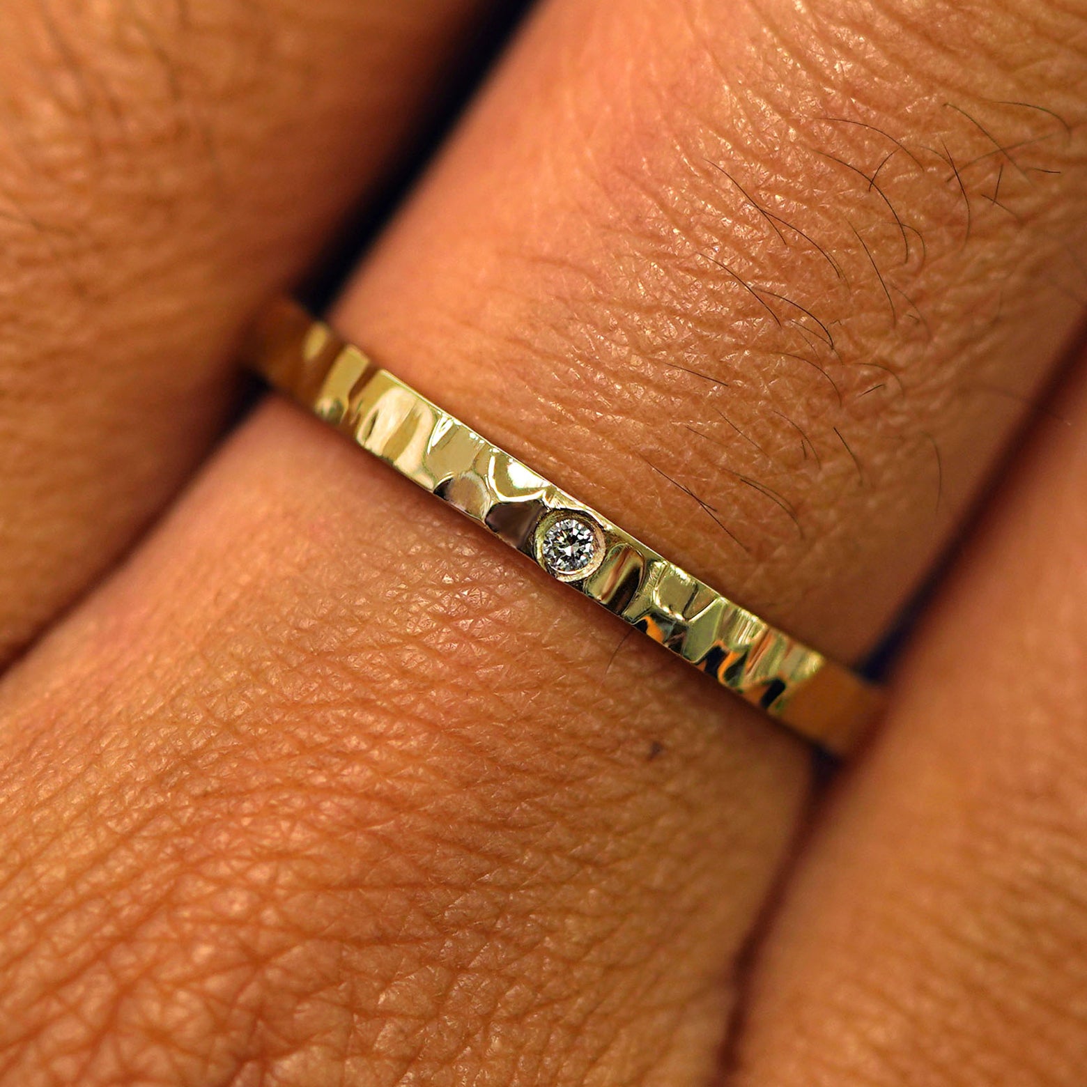 Close up view of a model's hand wearing a solid yellow gold Industrial Hammered Band with one diamond