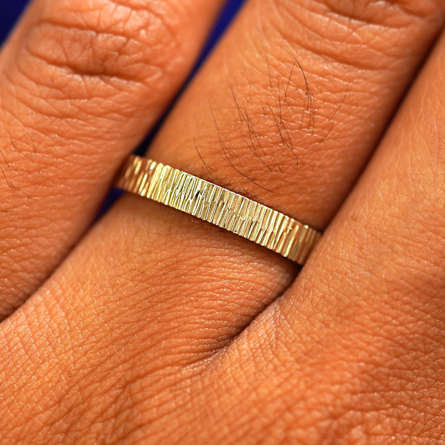 Close up view of a model's fingers wearing a 14k yellow gold Industrial Wood Band