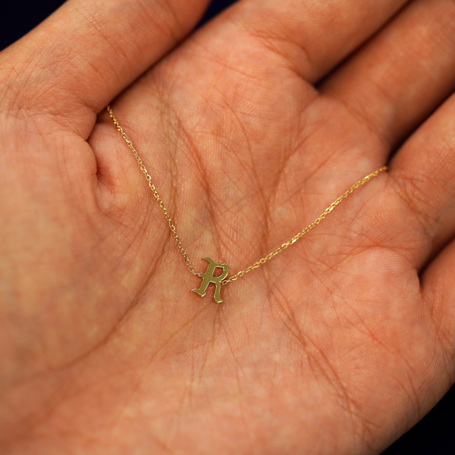 A solid 14k gold Initial Bracelet with the letter R draped resting in a models palm