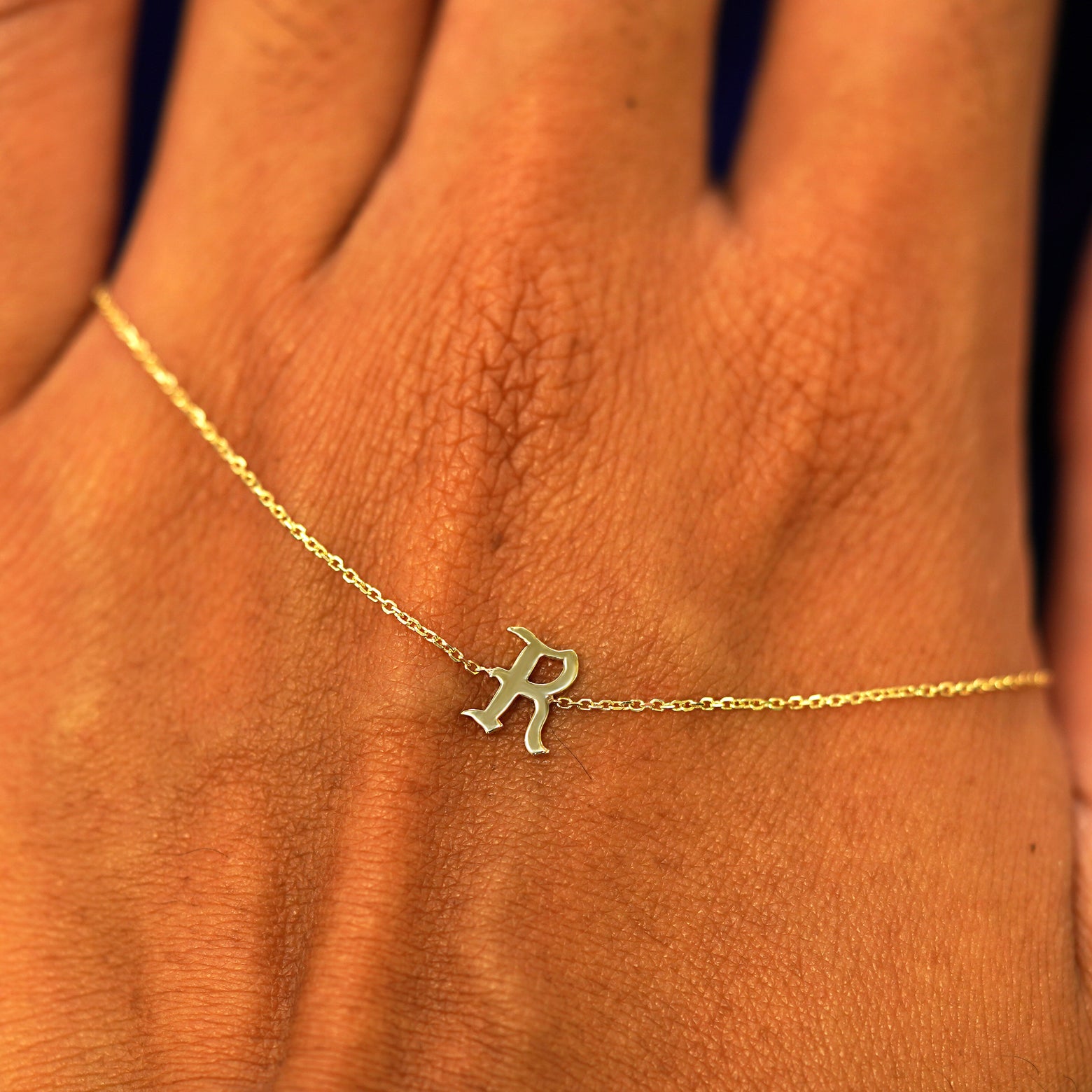 A solid 14k gold Initial Bracelet with the letter R draped across the back of a model's hand