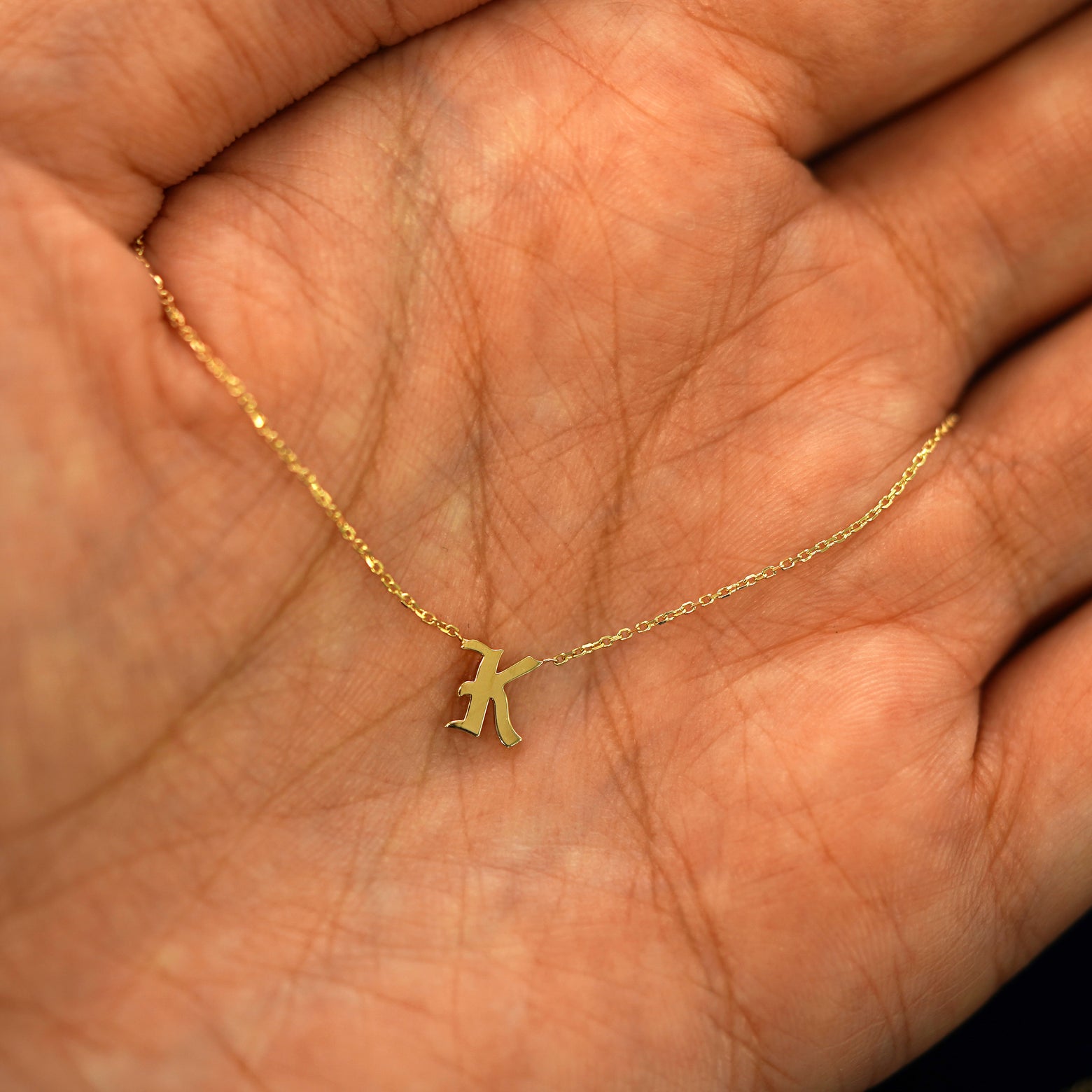 A solid 14k gold Initial Necklace with the letter K draped resting in a models palm