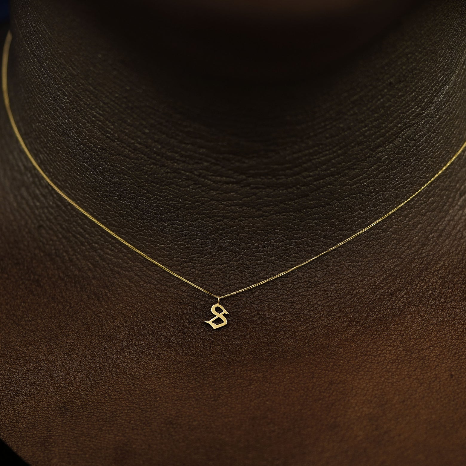 A model's neck wearing a 14k solid yellow gold Initial Charm Necklace in the letter S