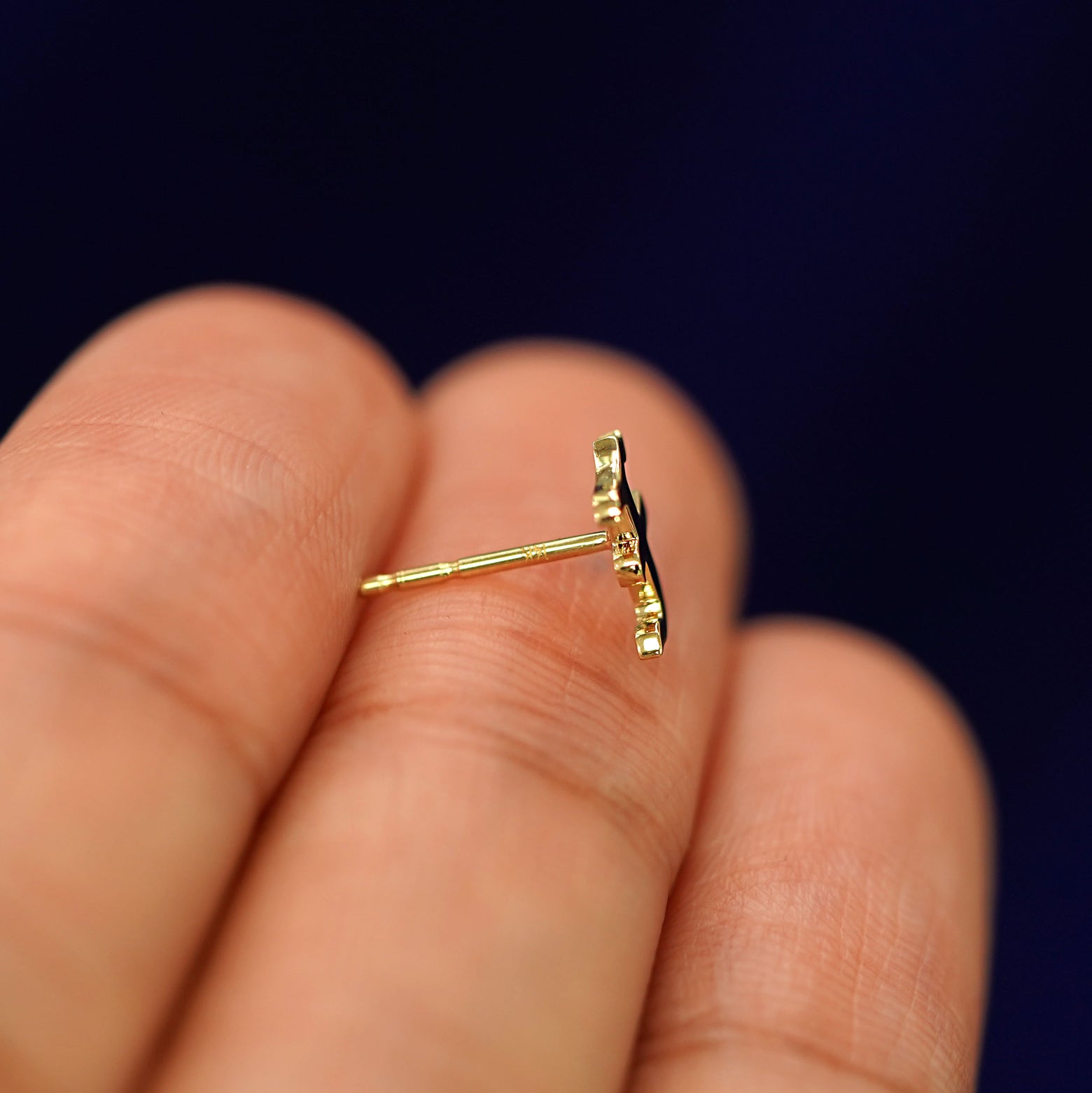 A 14k gold letter F Initial Earring resting sideways on a model's fingertip to show the pushback post without a backing