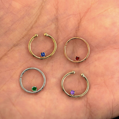 Four versions of the Raised Gemstone Septum shown in options of yellow, white, rose and champagne gold in a model's palm