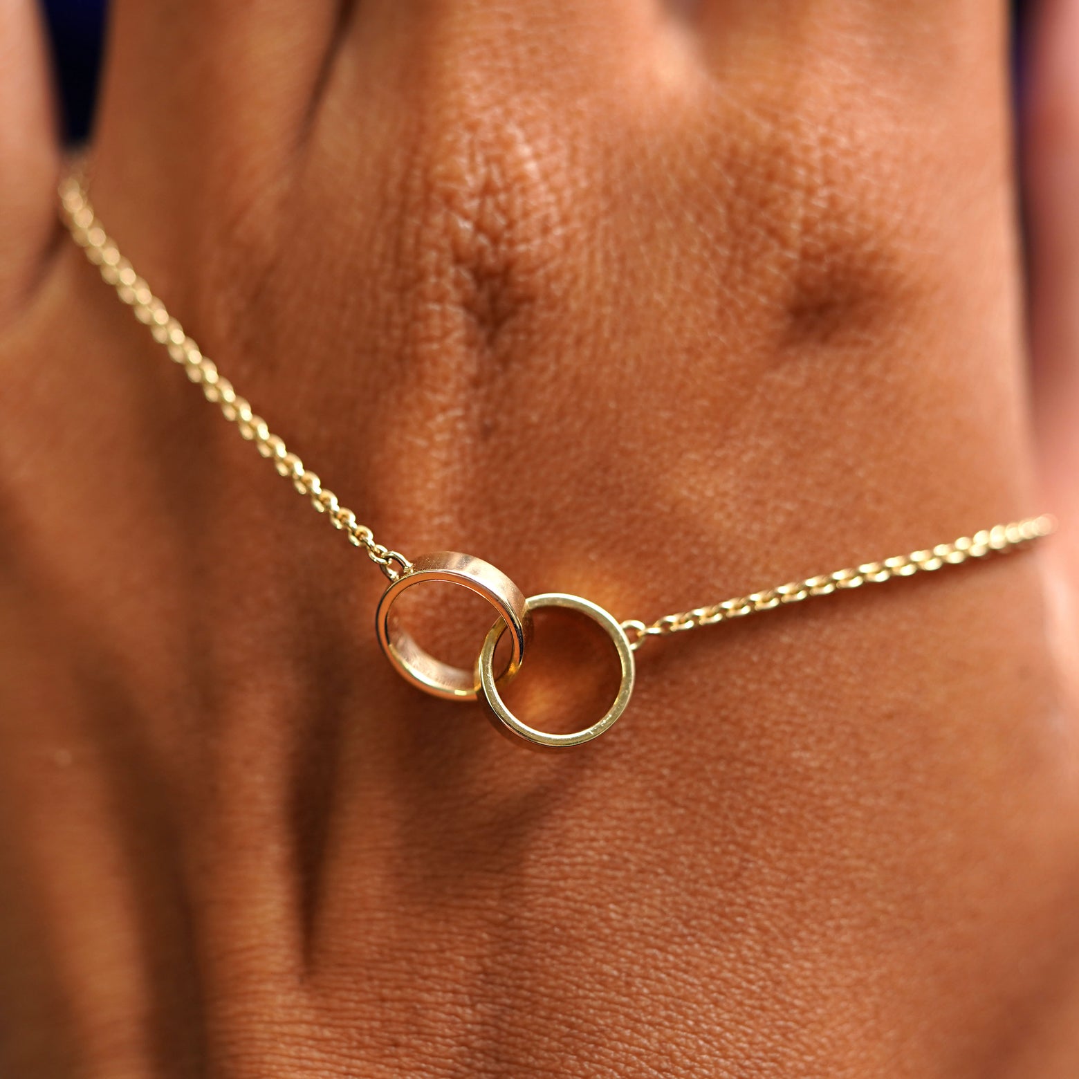 A solid gold Bound Together Necklace resting on the back of a model's hand
