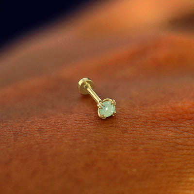 A solid 14k yellow gold Jade Flatback Piercing resting on the back of a model's hand