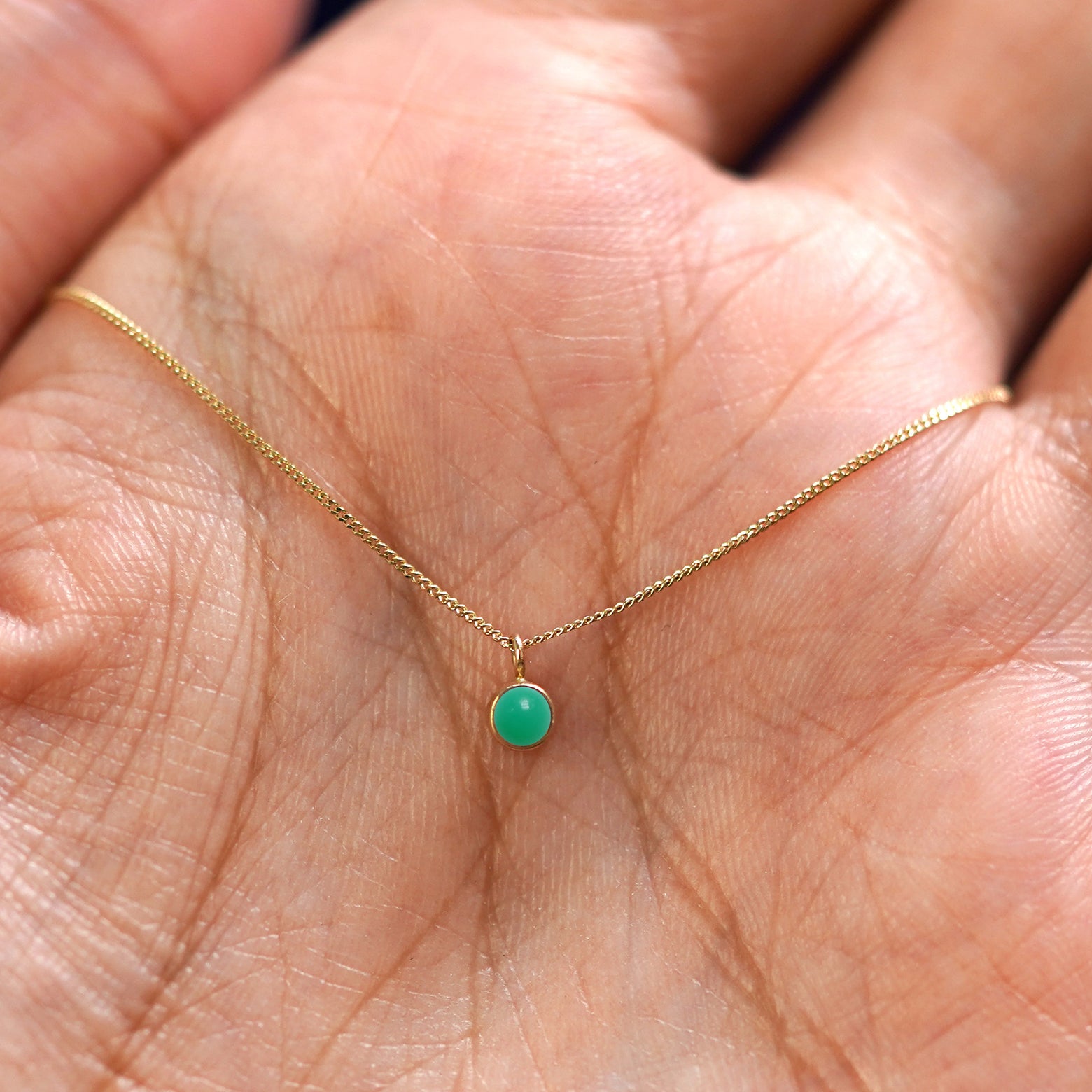 A solid 14k gold Jade Necklace resting in a models palm