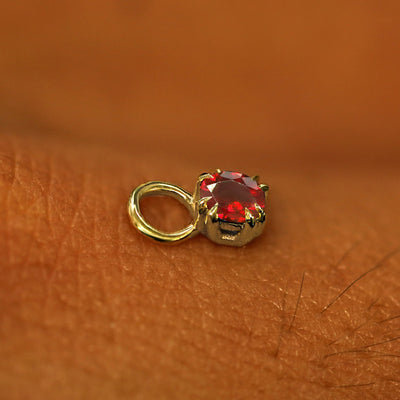 A solid yellow gold Garnet Charm for earring resting on the back of a model's hand