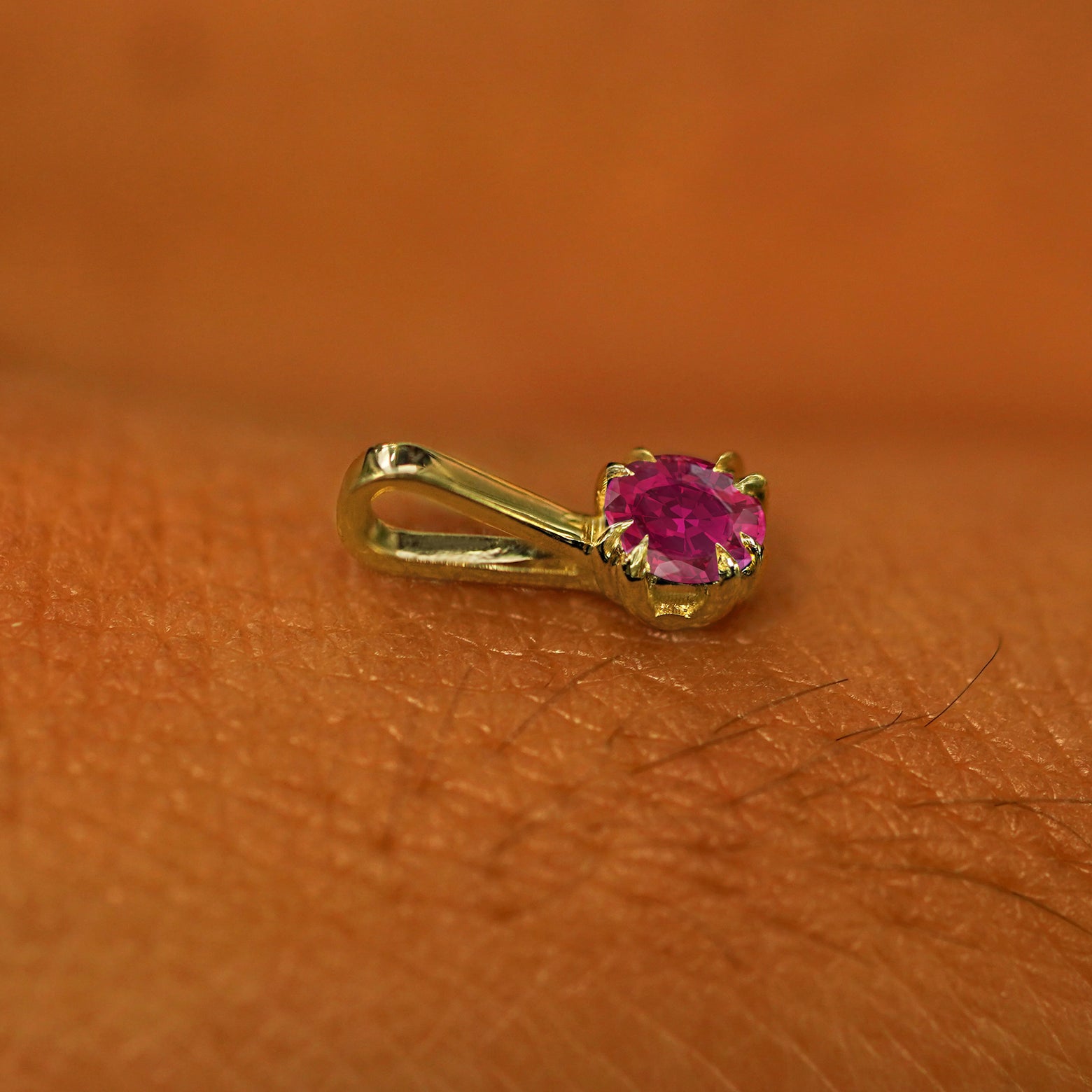 A 14k yellow gold Ruby Charm for chain resting on the back of a model's hand