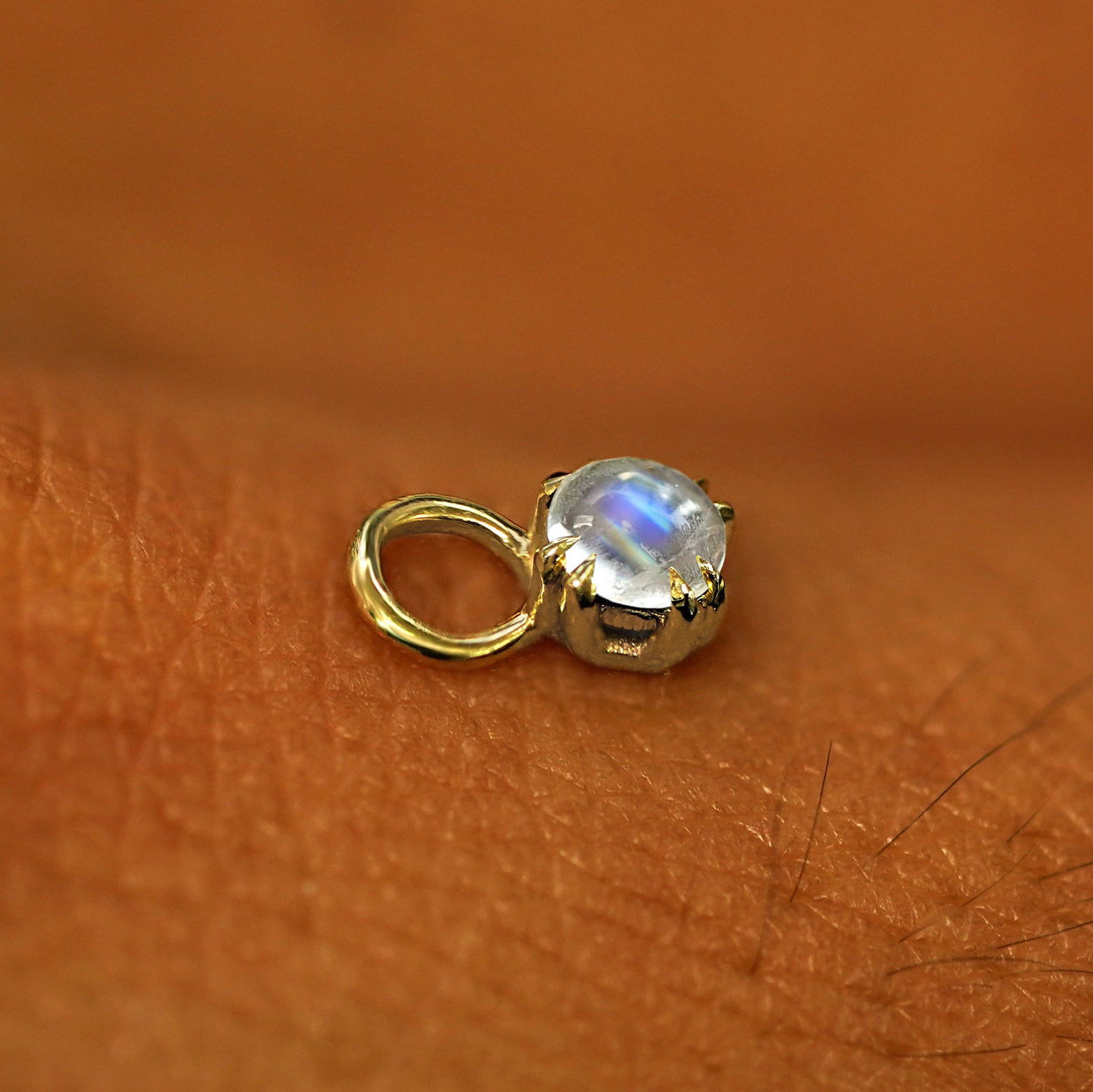 A solid yellow gold Moonstone Charm for earring resting on the back of a model's hand