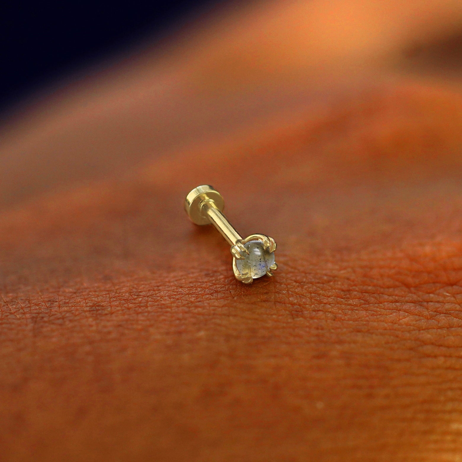 A solid 14k yellow gold Jade Flatback Piercing resting on the back of a model's hand