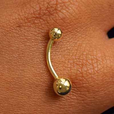 Close up view of a 14 karat gold Large Curved Barbell Piercing resting on the back of a model's hand