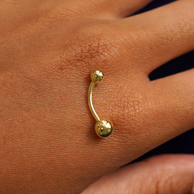 A yellow gold Large Curved Barbell Piercing resting on the back of a model's hand