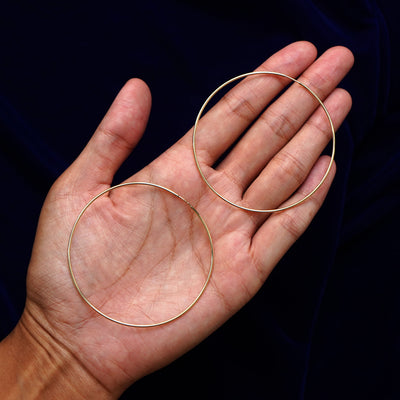 A pair of 14k gold Large Endless Hoop Earring sitting in a model's palm