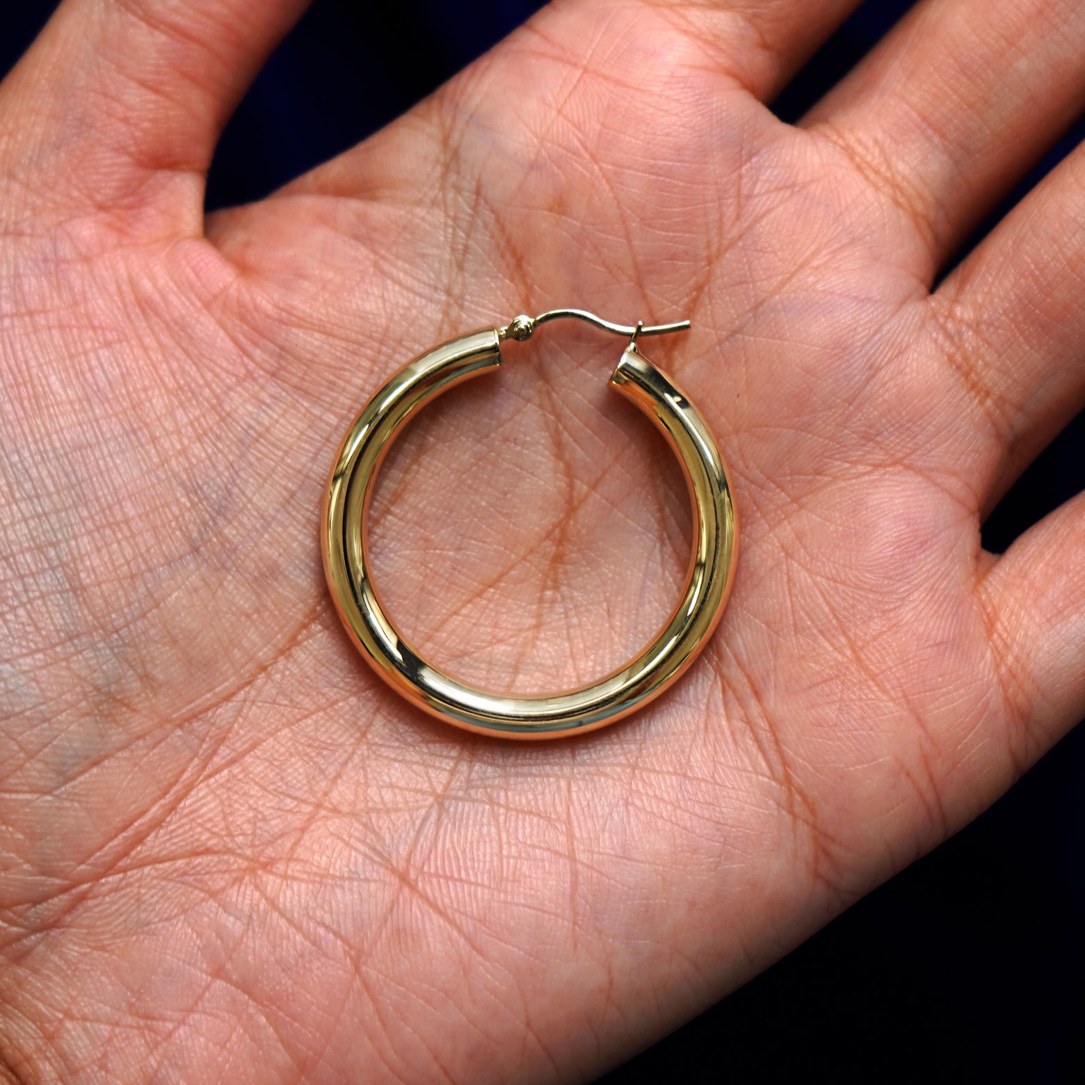 A solid 14k yellow gold Large Tube Hoop Earring closed in a model's palm