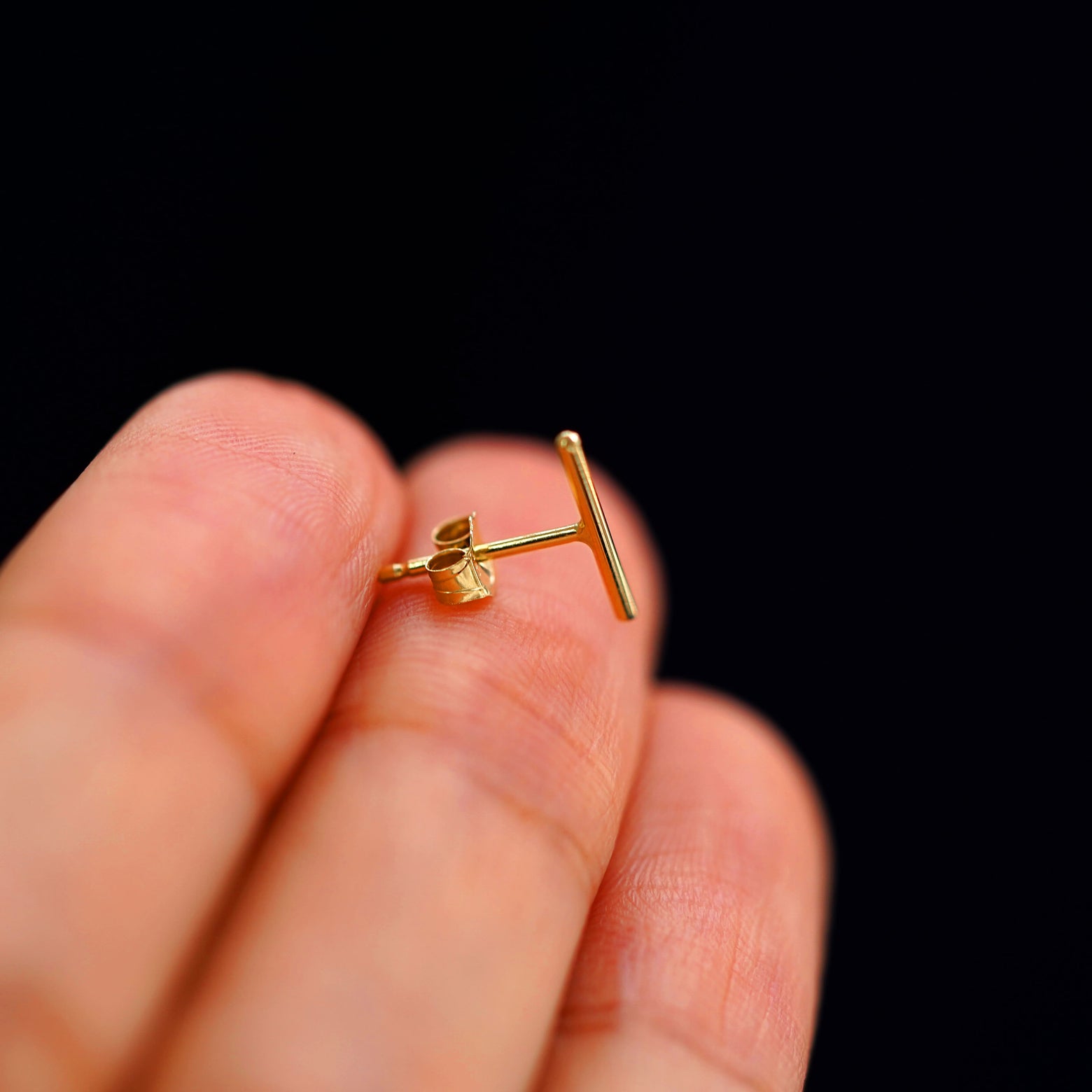 A 14k gold Large Line Earring sitting sideways on a model's fingertips to show detail