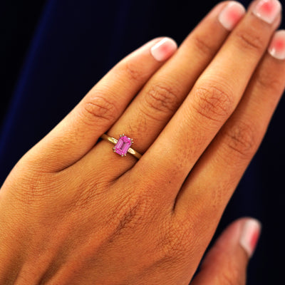 Close up view of a model's hand wearing a yellow gold Emerald Cut Pink Sapphire Ring on their finger