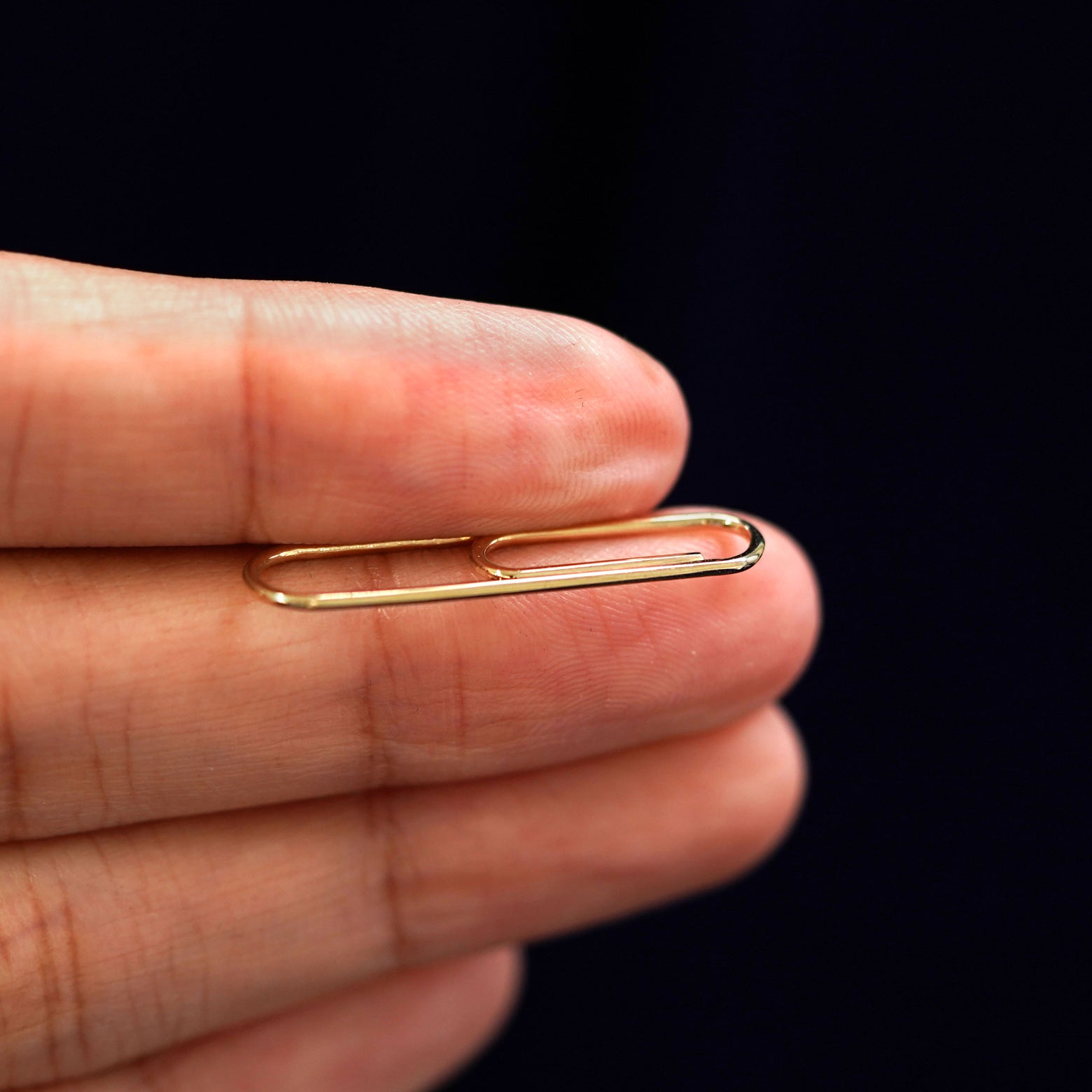 A yellow gold Not A Paper Clip Earring held between a model's fingers to show the thickness of the earring