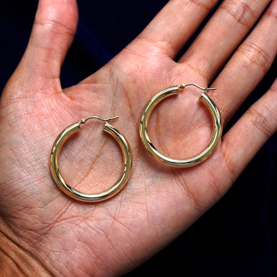 A pair of 14k gold Large Tube Hoop Earring sitting in a model's palm