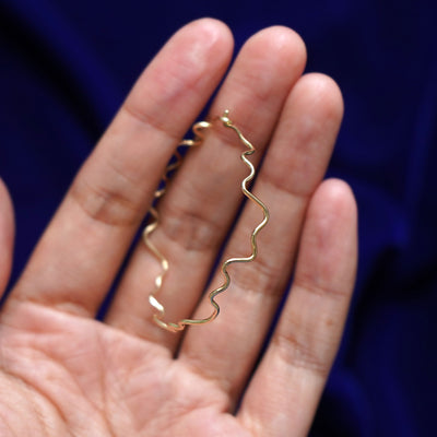 A 14k gold Large Wave Hoop Earring held in between a model's fingers to show the hoops thickness