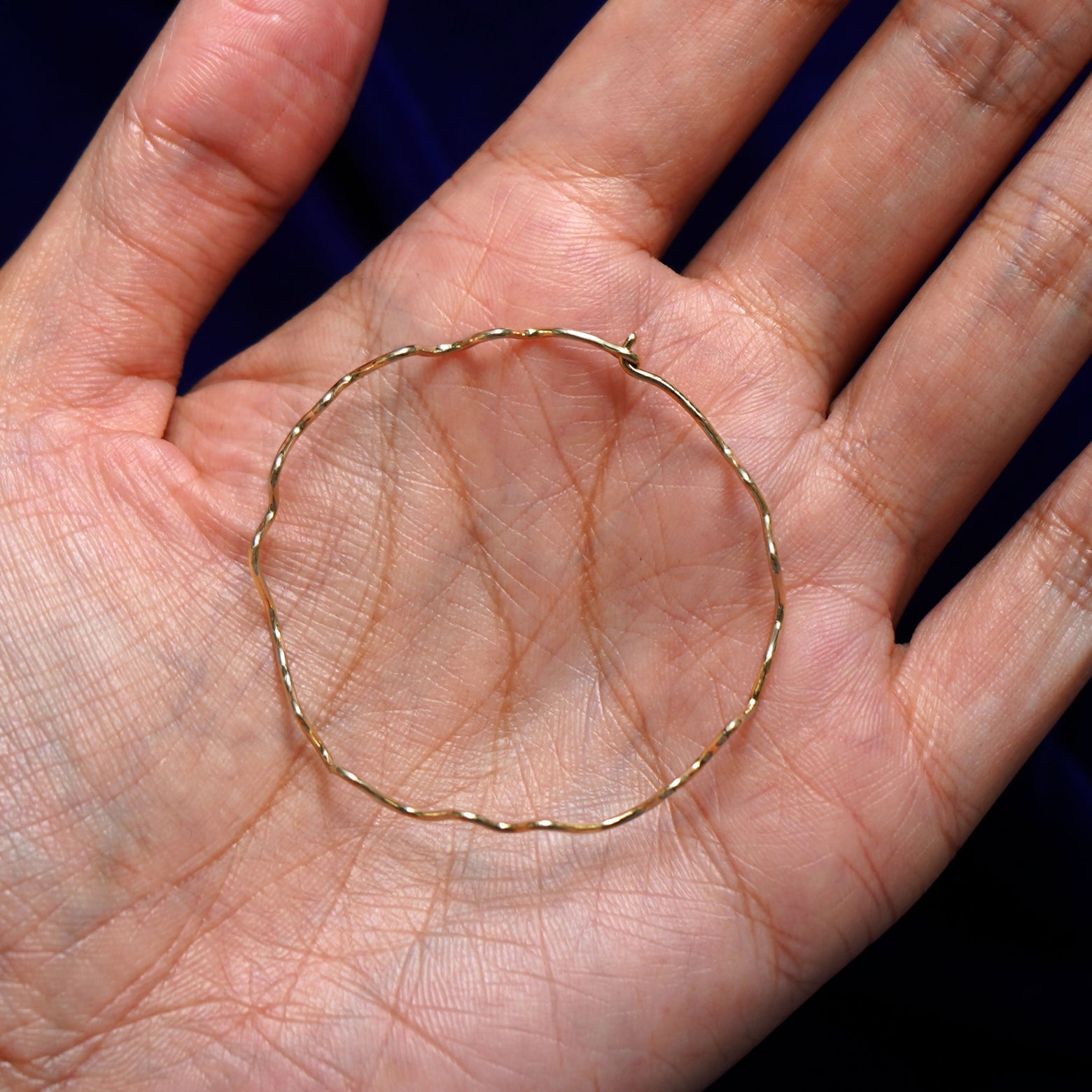 A solid 14k yellow gold Large Wave Hoop Earring closed in a model's palm