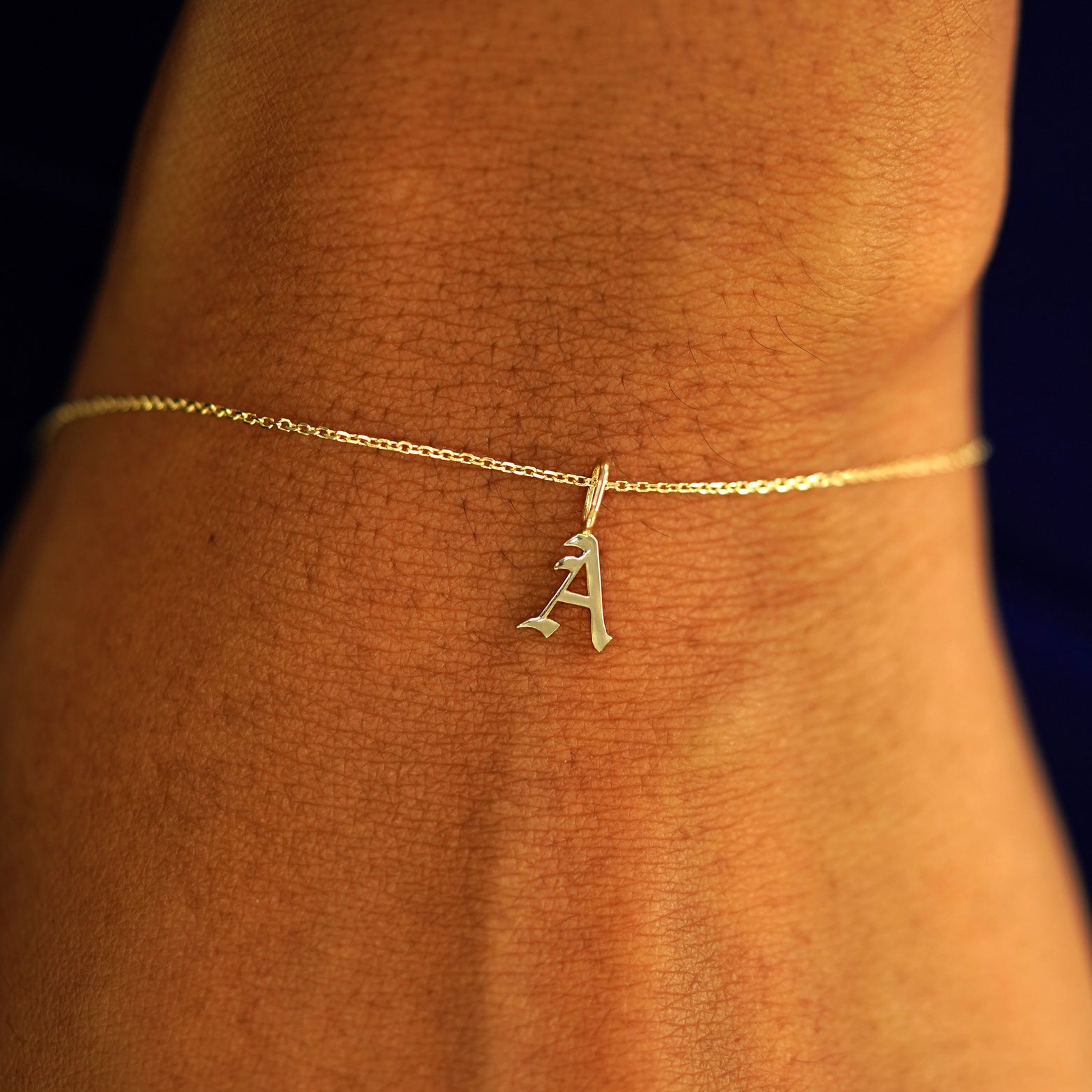 Close up view of a model's wrist wearing a 14k gold letter A Initial Charm on a Cable Bracelet
