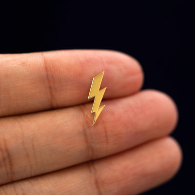 A solid 14k yellow gold Lightning Bolt Earring in between a model's fingers